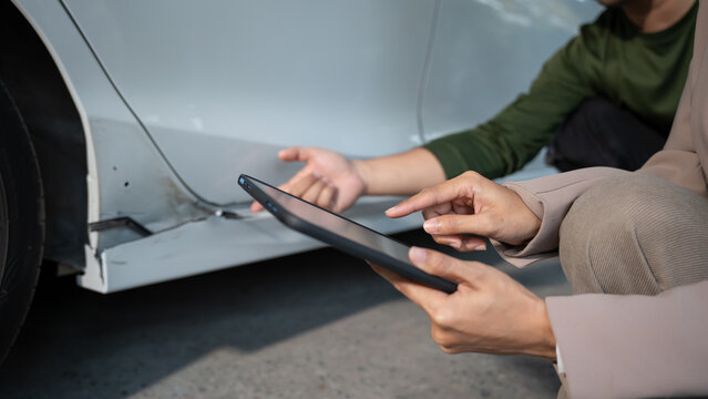 Close-up of people inspecting car body damage using a tablet beside a vehicle, suggesting auto repair assessment, insurance claim, and roadside assistance.