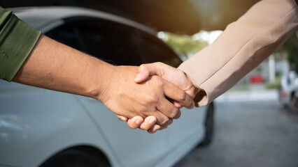 Close-up handshake between two people next to a white car, suggesting agreement during vehicle sale...