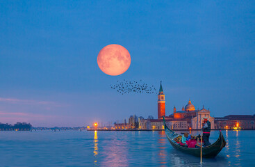 View of San Giorgio Island in Venice with wooden buoys in Giudecca Canal with full moon - Venetian gondolier punting gondola through canal waters at night - Venice Italy © muratart