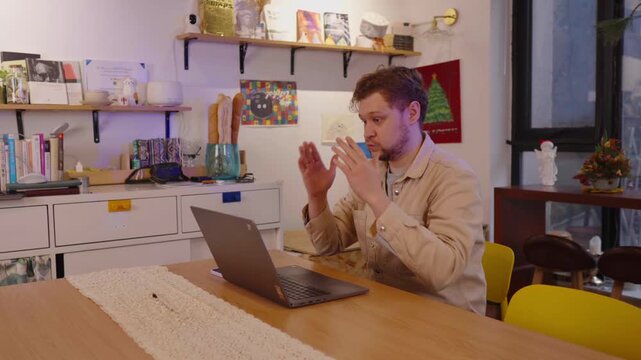 Frustrated and overworked man getting angry during a difficult video conference while working on laptop from home, showing signs of stress, professional burnout and anxiety