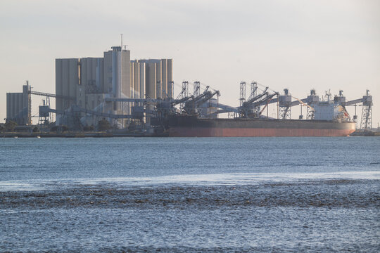 View of a large bulk carrier cargo ship docked at an industrial terminal with grain silos and loading cranes in Lisbon, Lisbon, Portugal.