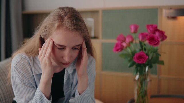 Millennial woman lady massaging her temples in her living room, experiencing financial risk, exhausted and overwhelmed, experiencing a debilitating headache, brain fog and financial risk