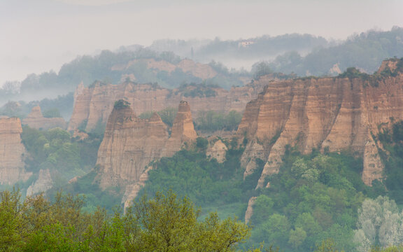 View of the Balze del Valdarno erosion formations surrounded by lush green vegetation and misty hills in Piantravigne, Tuscany, Italy.