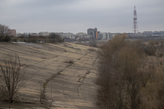 Wide view of a weathered concrete slope at the edge of a natural area with a city skyline and radio tower in the distance