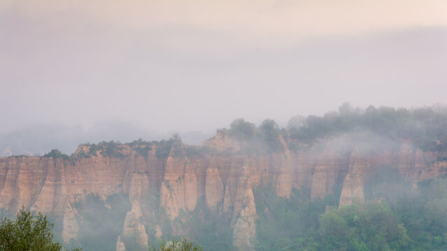 View of the Balze del Valdarno erosion formations shrouded in morning mist with green trees and a soft sky Piantravigne, Tuscany, Italy.