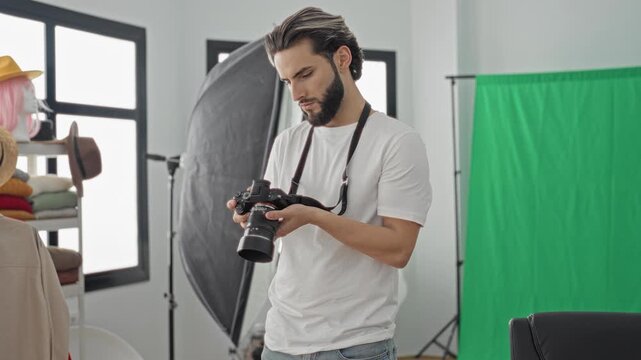 Man holding dslr camera checking settings and rubbing forehead amid green screen, softbox and mannequin in studio; quiet contemplation.
