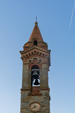 View of the historic stone bell tower featuring a clock and two bells against a clear blue sky in Piantravigne, Tuscany, Italy.