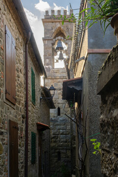 View of the historic stone bell tower and narrow medieval alleyway with traditional wooden shutters in Loro Ciuffenna, Tuscany, Italy.