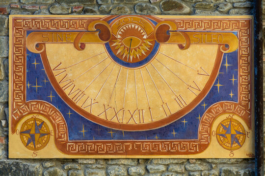 View of a colorful painted sundial with Roman numerals and a sun motif on an ancient stone wall in Loro Ciuffenna, Tuscany, Italy.