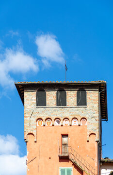 View of the historic medieval tower with heraldic shields and stone masonry under a bright blue sky in Loro Ciuffenna, Tuscany, Italy.