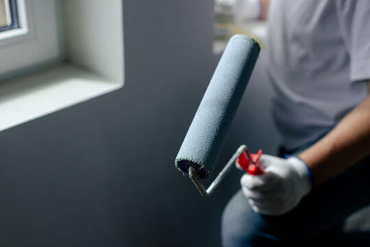 Hand holding paint roller applying gray paint