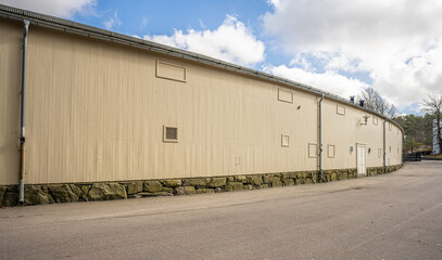 Fototapeta premium Long industrial warehouse building exterior with minimal windows and paved empty surroundings.