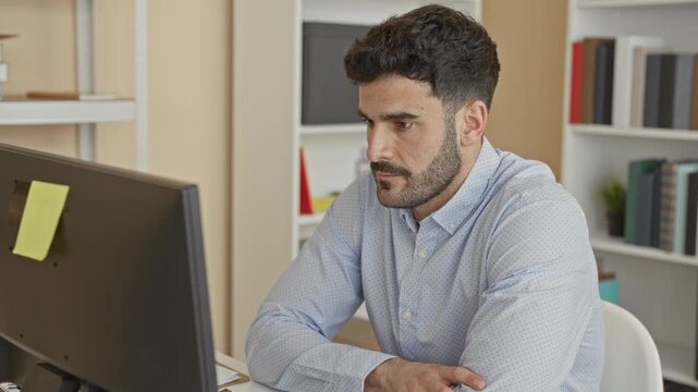 Man at computer with finger to lips performing shushing gesture in office building; quiet concentration.