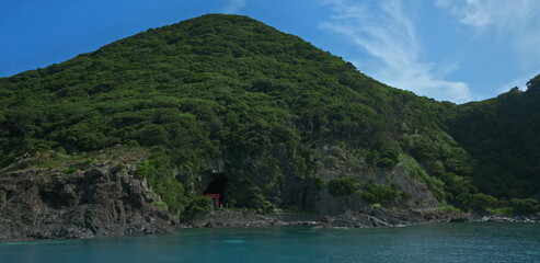 Obraz premium Coastal sea cave with red torii gate and lush green mountain slopes