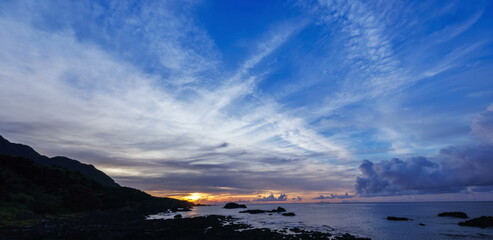 Obraz premium Bright morning sun rising over a rocky coast under a wide blue sky