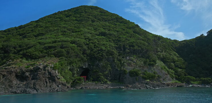 Coastal sea cave with red torii gate and lush green mountain slopes