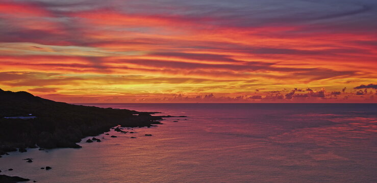 Golden sunset glow over dark coastal silhouettes and calm ocean water