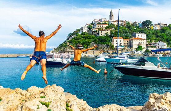 ather and son jumping into the sea in vrbnik harbour croatia. Joyful, summer vacation concept