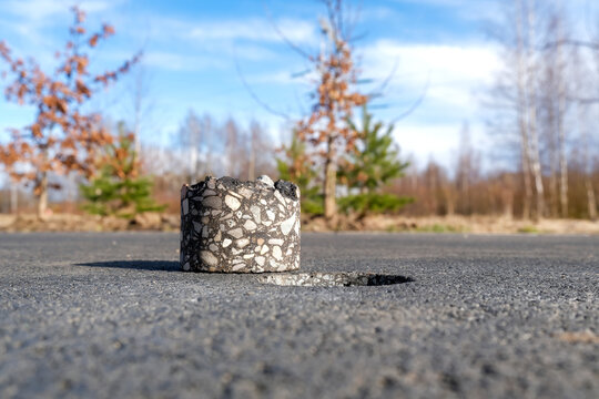 Close-up of an asphalt core sample taken from a road surface with a drilled hole nearby. Road testing process