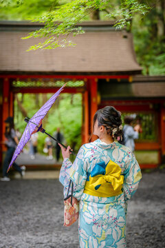 Back view of one woman wearing Japanese yukata summer kimono and holding Japanese traditional oil paper umbrella in Kifune Shrine nature forest gate, Kyoto, Japan.