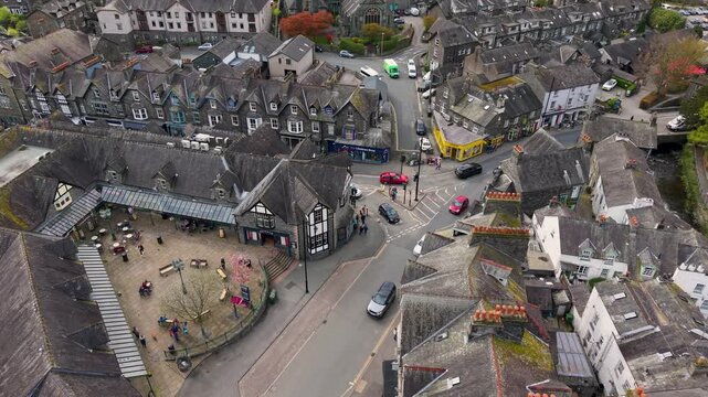 A static aerial drone shot over Ambleside town centre, Cumbria, capturing the market square, Kelsick Centre, Rydal Road and the busy A591 junction with surrounding slate rooftops.