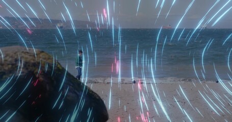 Fototapeta premium Standing child in green hooded jacket facing waves at shore, mossy rock and cyan-magenta streaks