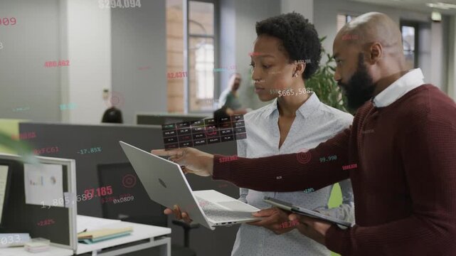 Woman holding laptop man tapping tablet causing floating finance charts showing data driving choice