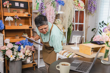 Fototapeta premium Asian senior woman, florist, small business owner, entrepreneur checking stock of decorative flowers in shop, showing independent business lifestyle, creative workspace, passion, and customer service