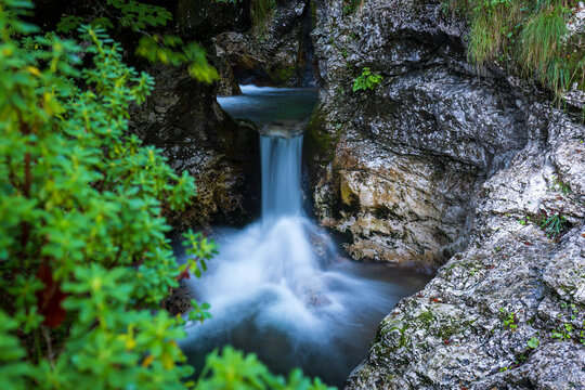 10 September 2022: View of a small waterfall cascading between mossy rocks and lush green foliage in a secluded forest ravine.