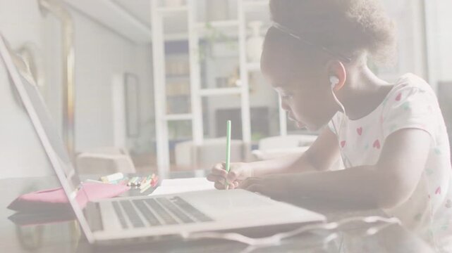 Girl student glancing at laptop and writing on worksheet at home, using green pencil for study