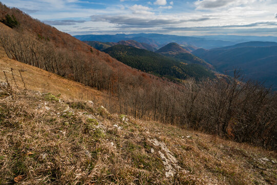 View of Kozi chrbat mountain peak with autumnal forests and rolling hills under a cloudy sky in Mostenica, Banska Bystrica Region, Slovakia.