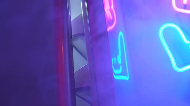 Slow pan tracking shot of neon sign reflections sliding across glass panels revealing spiral staircase in indoor studio