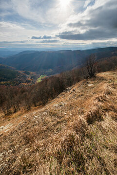 View of Kozi chrbat mountain with grassy slopes and autumn forests under sunbeams breaking through clouds in Mostenica, Banska Bystrica Region, Slovakia.