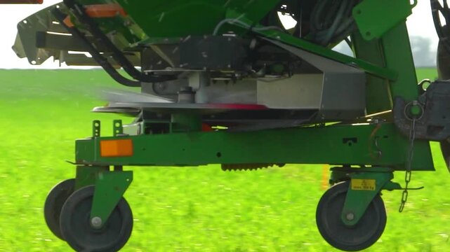 Close-up footage of fertilizer spreader dispersing granules on green field, agricultural machinery in motion, crop nutrition process
