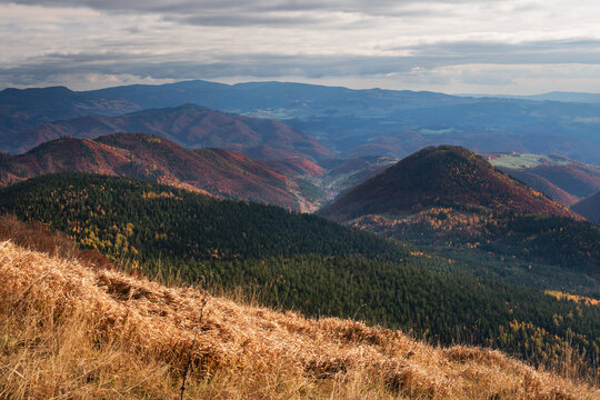 View of Kozi chrbat mountain ridge overlooking rolling hills covered in autumn forests under a cloudy sky in Mostenica, Banska Bystrica Regio, Slovakia.