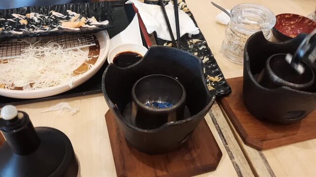 A person carefully extinguishing the blue flame of a solid fuel gel (sterno) inside a portable grill after finishing a meal.