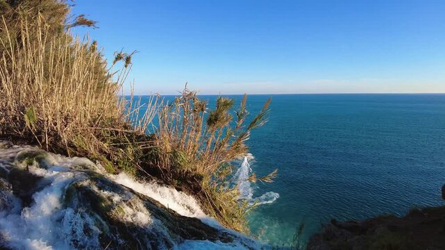 4K Top of Lower D&uuml;den Waterfall with water flowing over rocks into the sea in Antalya, Turkey. Airplane flying in the sky and boat moving across the Mediterranean with natural water sounds