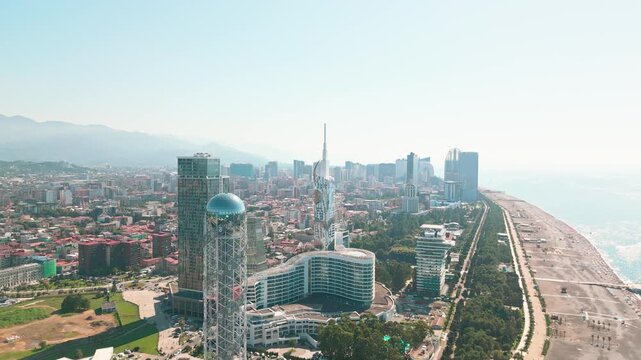 aerial view of the Batumi waterfront in Georgia, featuring the iconic Alphabetic Tower, the modern city skyline, and the long pebble beach coastline along the Black Sea under a clear sky