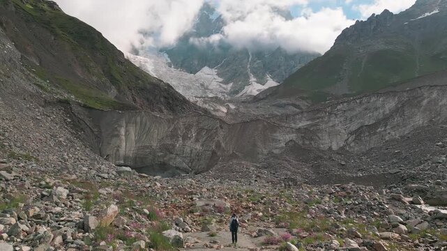 Aerial view woman Hiker reaching walk up overlooking Shkhara glacier in Svaneti region.. Massive snow-capped Mount Shkhara peaks dominate horizon. Upper Svaneti alpine landscape near Ushguli, Georgia.