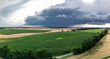 Panoramiczny widok na malownicze pola uprawne pod dramatycznym, zachmurzonym niebem. Nad horyzontem widoczne lokalne opady deszczu. Wiejski krajobraz rolniczy w letni dzień przed burzą. © Henryk Niestrój