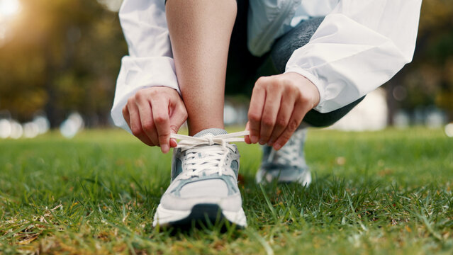 Person, hands and tying with shoes on grass field for fitness, workout preparation or run in nature. Active, runner or getting ready with sneakers or laces for outdoor exercise or training in park