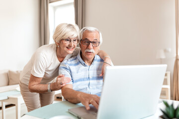 Fototapeta premium Senior woman embracing her husband while video calling grandchildren on laptop. Happy elderly couple talking to family online. Retirement lifestyle, family love, and technology proficiency concept.