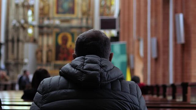 Anonymous man sitting on a pew and praying inside a beautiful catholic church. A religious parishioner is seeking solace and forgiveness during a solemn worship service at a cathedral