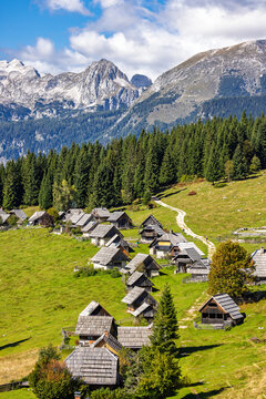 View of the traditional wooden shepherd huts at Planina Zajamniki on a green alpine meadow with pine forests and mountain peaks in Srednja vas v Bohinju, Radovljica, Slovenia.