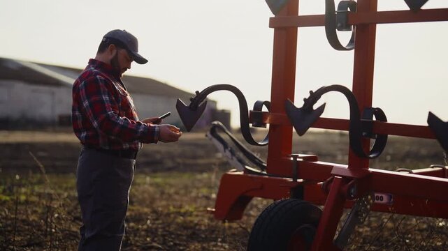 Agriculture and agribusiness, farmworker using smartphone, standing near tractor . Professional agronomist and farmer testing new mobile app for farming and control harvest, portrait in nature