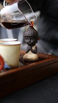 Slow motion pouring of hot dark puerh tea over a small buddha figurine during a traditional chinese gongfu cha tea ceremony, representing a moment of zen, relaxation, and spiritual culture