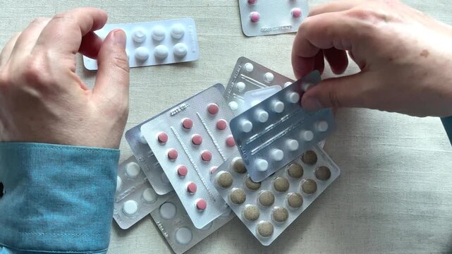 Elderly man hands sorting through blister packs of pills on a table. Healthcare, pharmacy, medication.