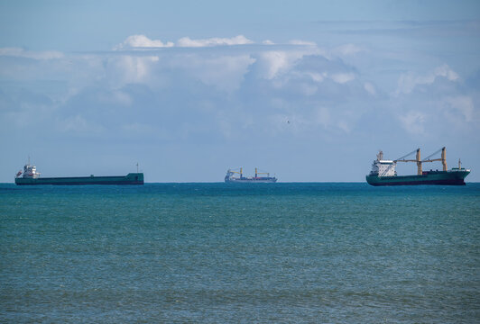 View of three cargo ships sailing on the calm blue sea under a bright cloudy sky.