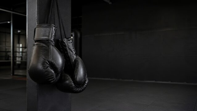 Black boxing gloves hanging in a dark gym with dramatic lighting.