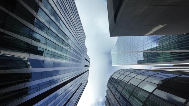 London's financial district skyline with modern glass skyscrapers reflecting the moving clouds. Worm's-eye view of the city's impressive corporate architecture and economy
